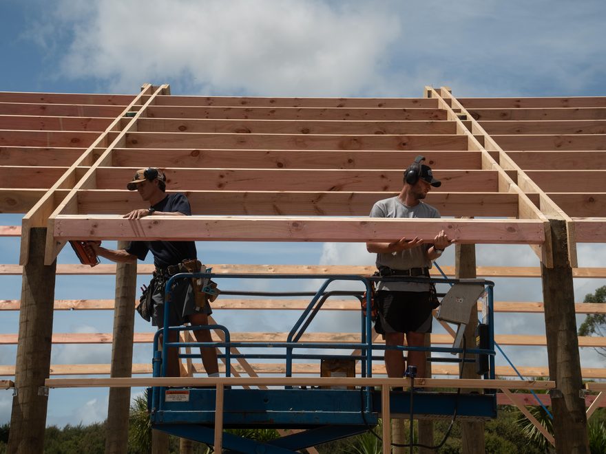 Two builders on a scissor lift fixing timber purlins to a pole shed roof frame