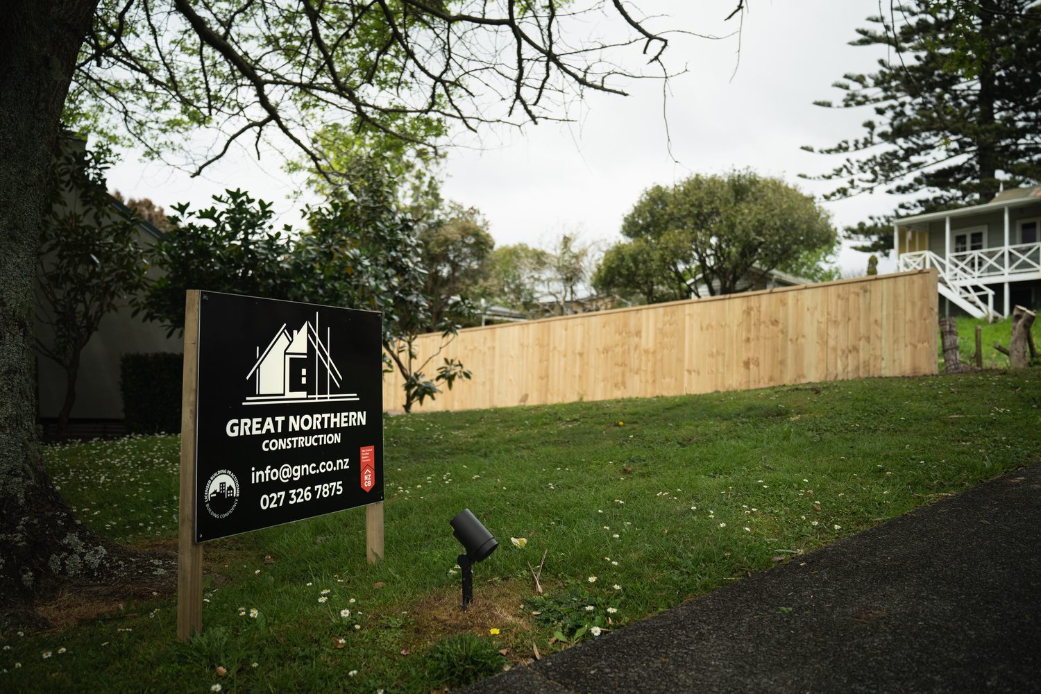 Builder's sign on a front lawn with a long paling fence and a white house behind