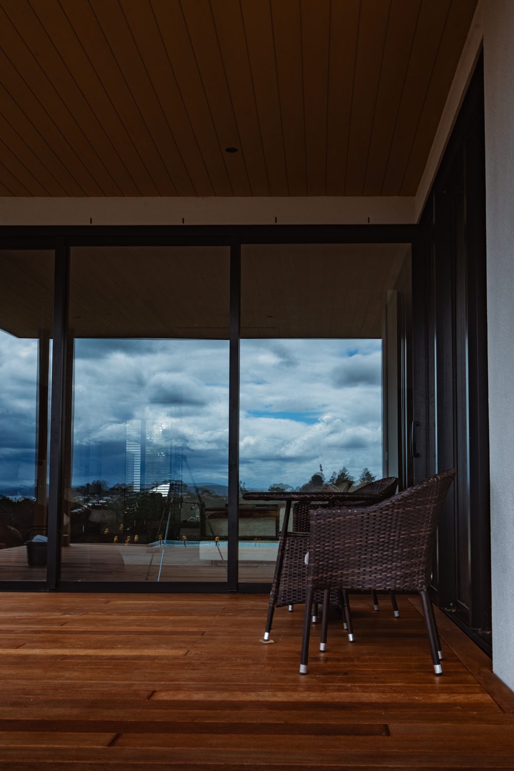 Hardwood deck under a covered roof, with tall sliding doors reflecting a cloudy sky