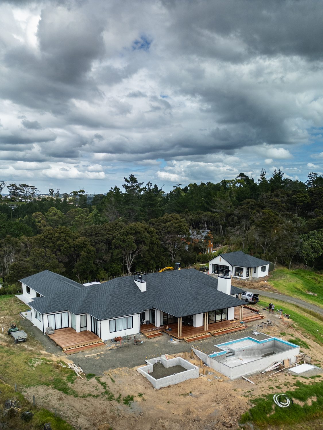 Completed home with a dark roof and timber decks against native bush, the pool still being formed
