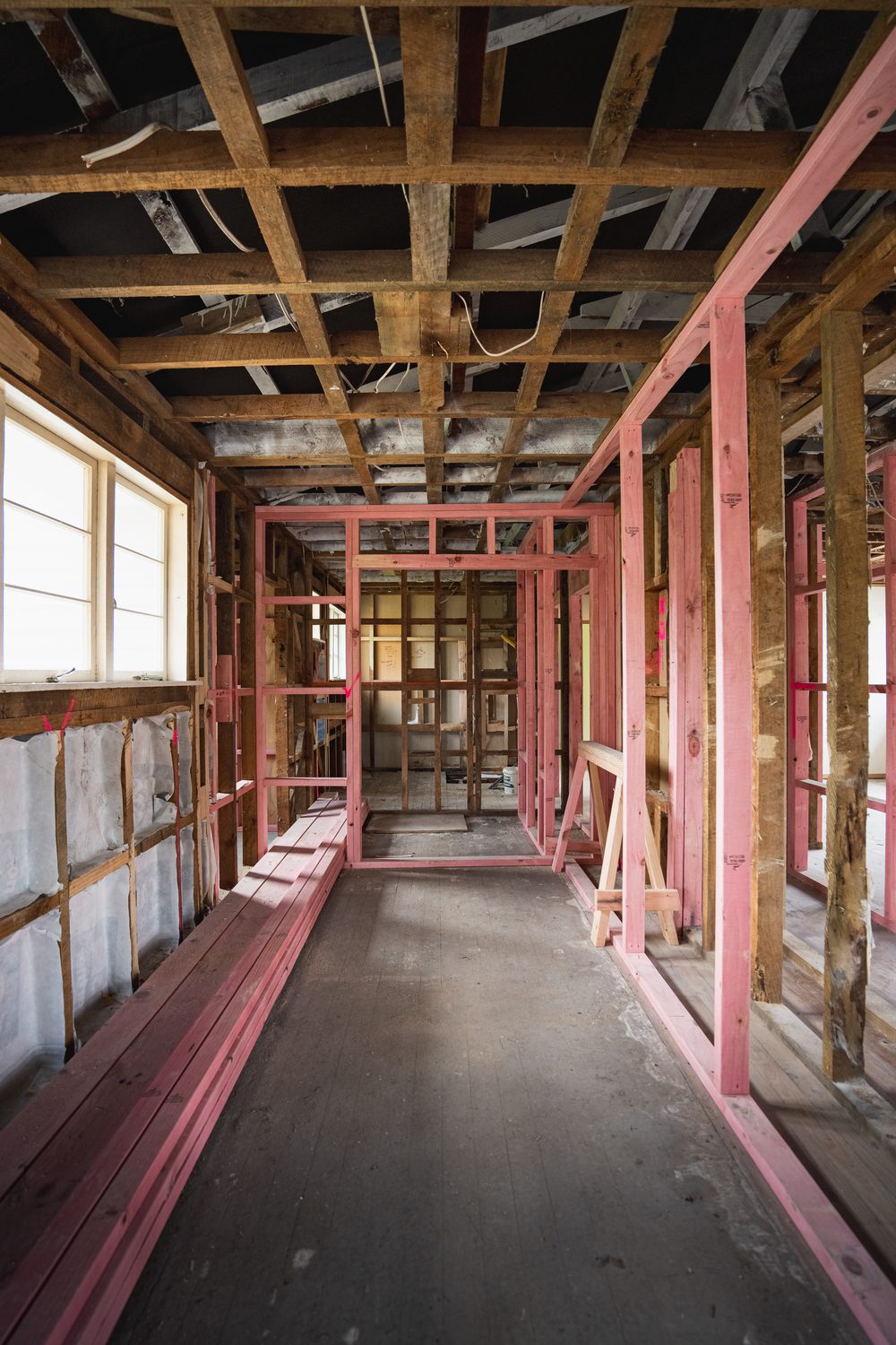 Hallway stripped to the studs, with new pink framing and insulation along one wall