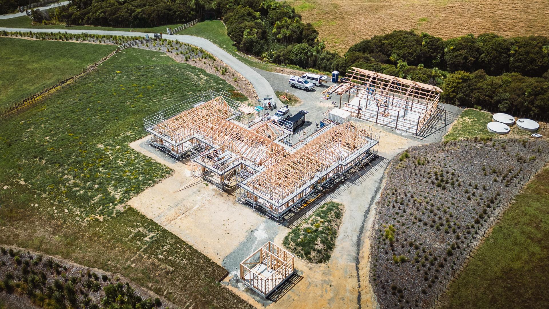 Drone view of a large house frame with roof trusses up and a garage frame beside it on a rural section