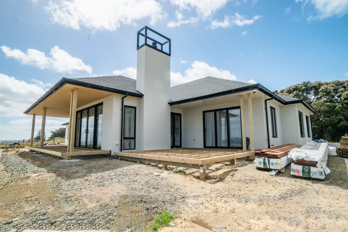 New white home with a tall chimney and covered porch, deck framing and packs of decking timber in front