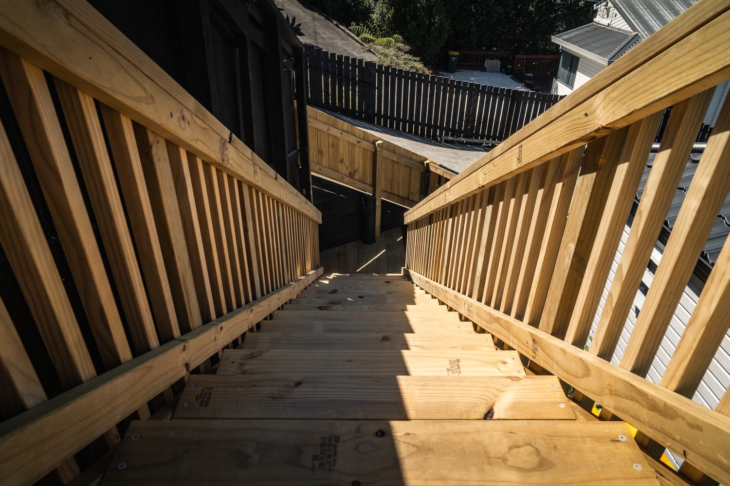 Looking down a flight of new timber stairs between slatted balustrades, sunlight across the treads