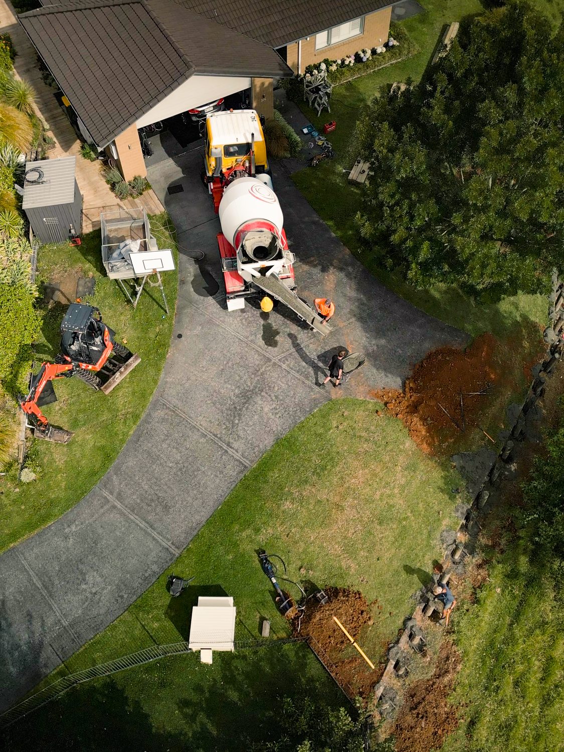 Drone view straight down on a concrete truck, a mini digger and a fresh trench beside a lawn