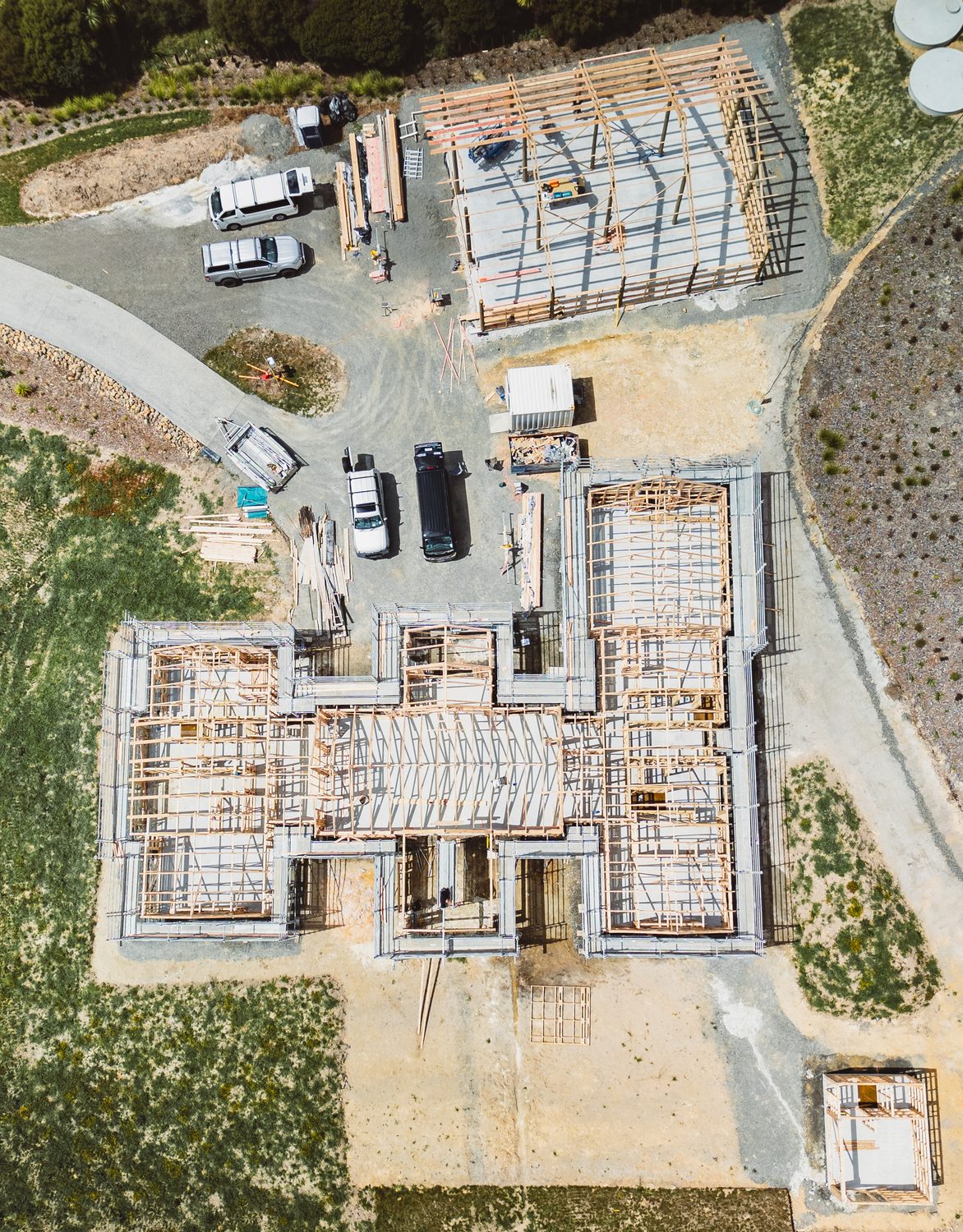 Straight-down drone view of a house frame, a garage frame and work vehicles on site