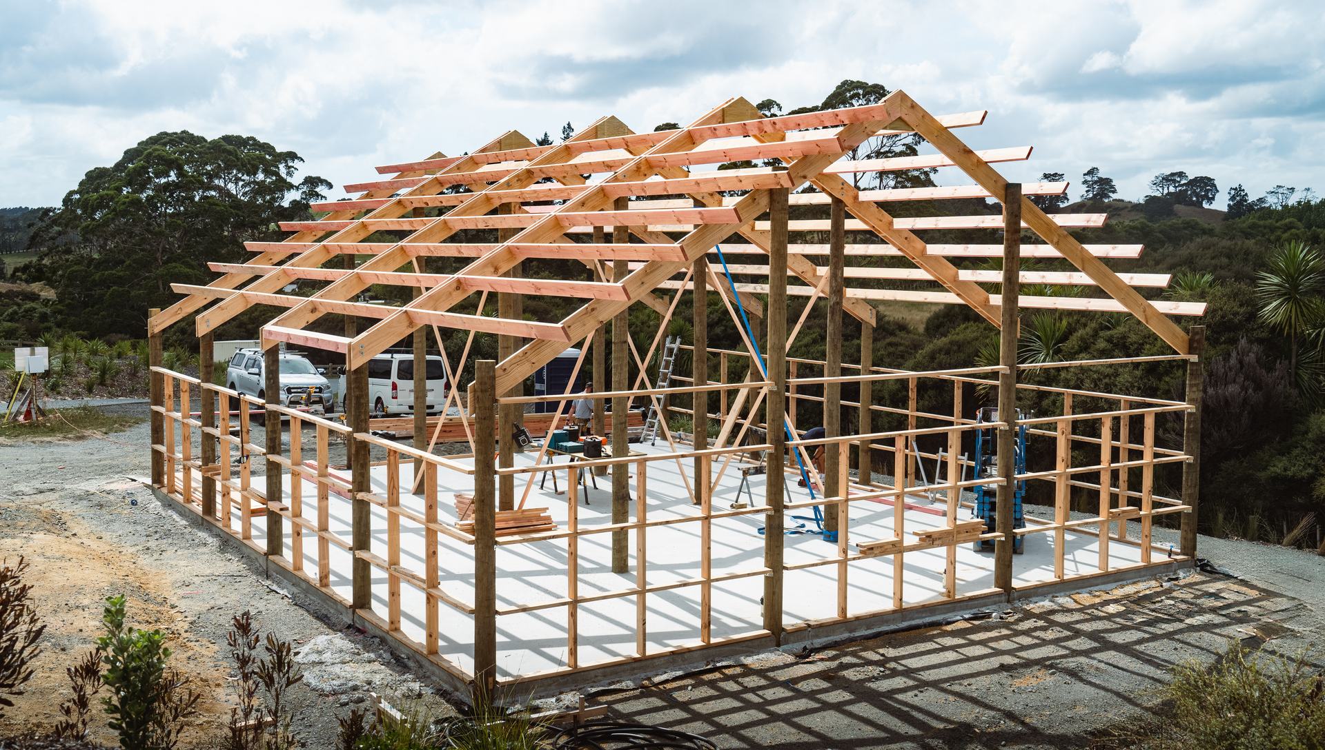 Pole shed under construction, with timber poles, roof trusses and purlins standing on a concrete slab