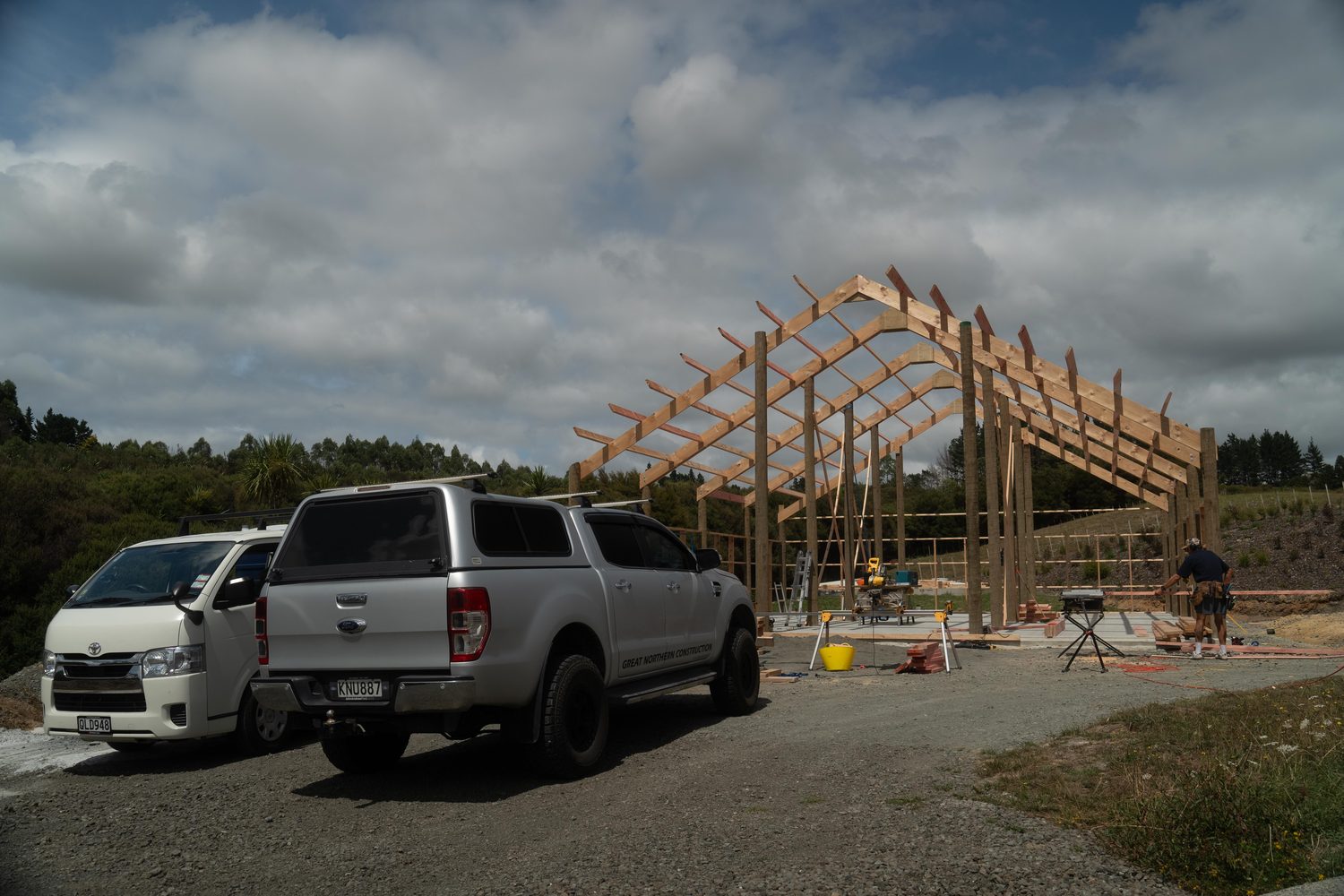 Van and ute parked on gravel in front of a tall pole shed frame