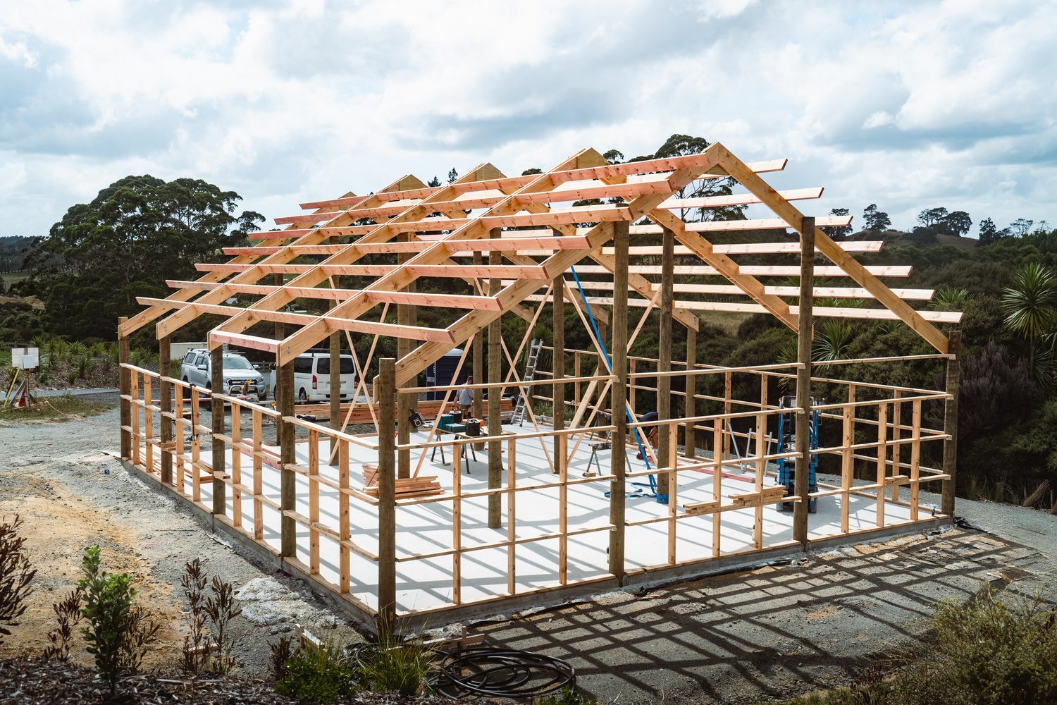 Gable roof trusses and timber poles of a shed frame on a white concrete slab