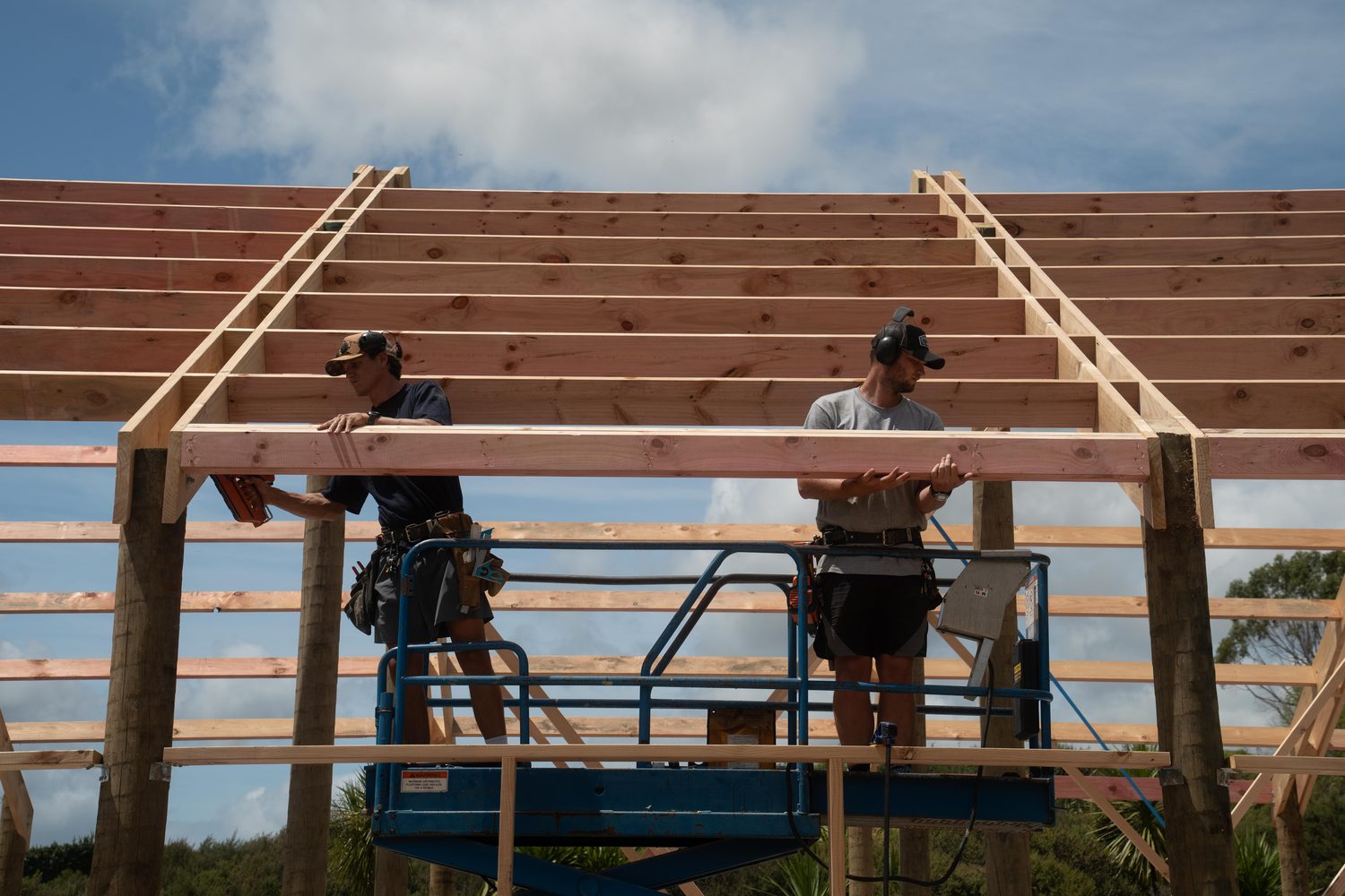 Builders on a blue scissor lift working on the roof purlins of a pole shed