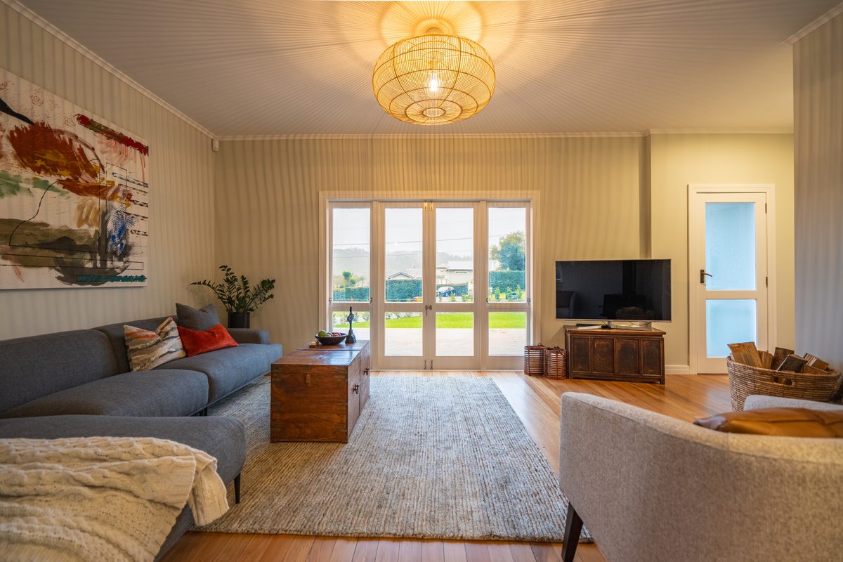 Lounge with a grey sofa, woven pendant light, timber floor and French doors opening onto a lawn
