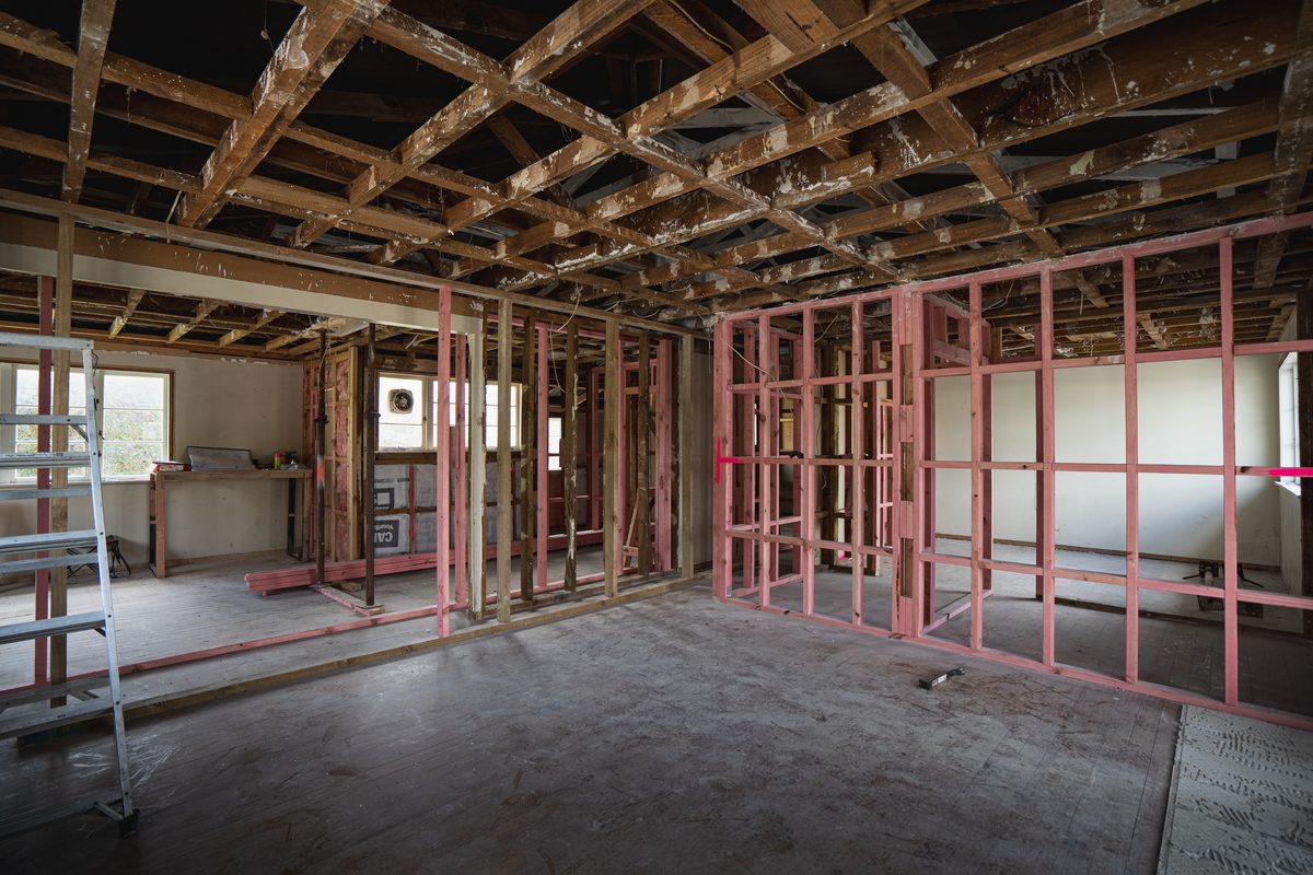 House interior stripped back to its framing, with new pink wall framing and the ceiling joists exposed