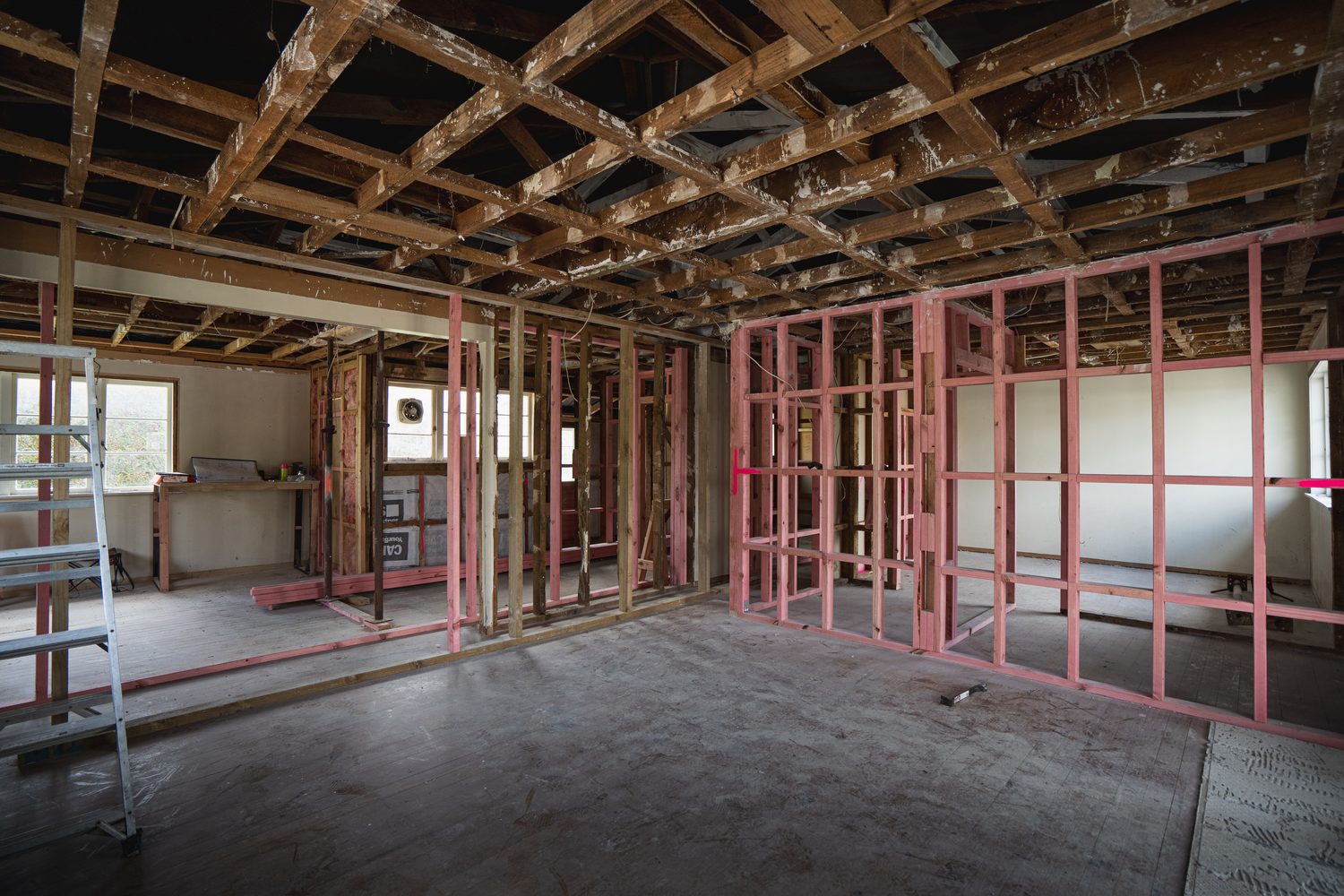 Open interior during a renovation, old ceiling framing exposed and new walls framed in pink timber