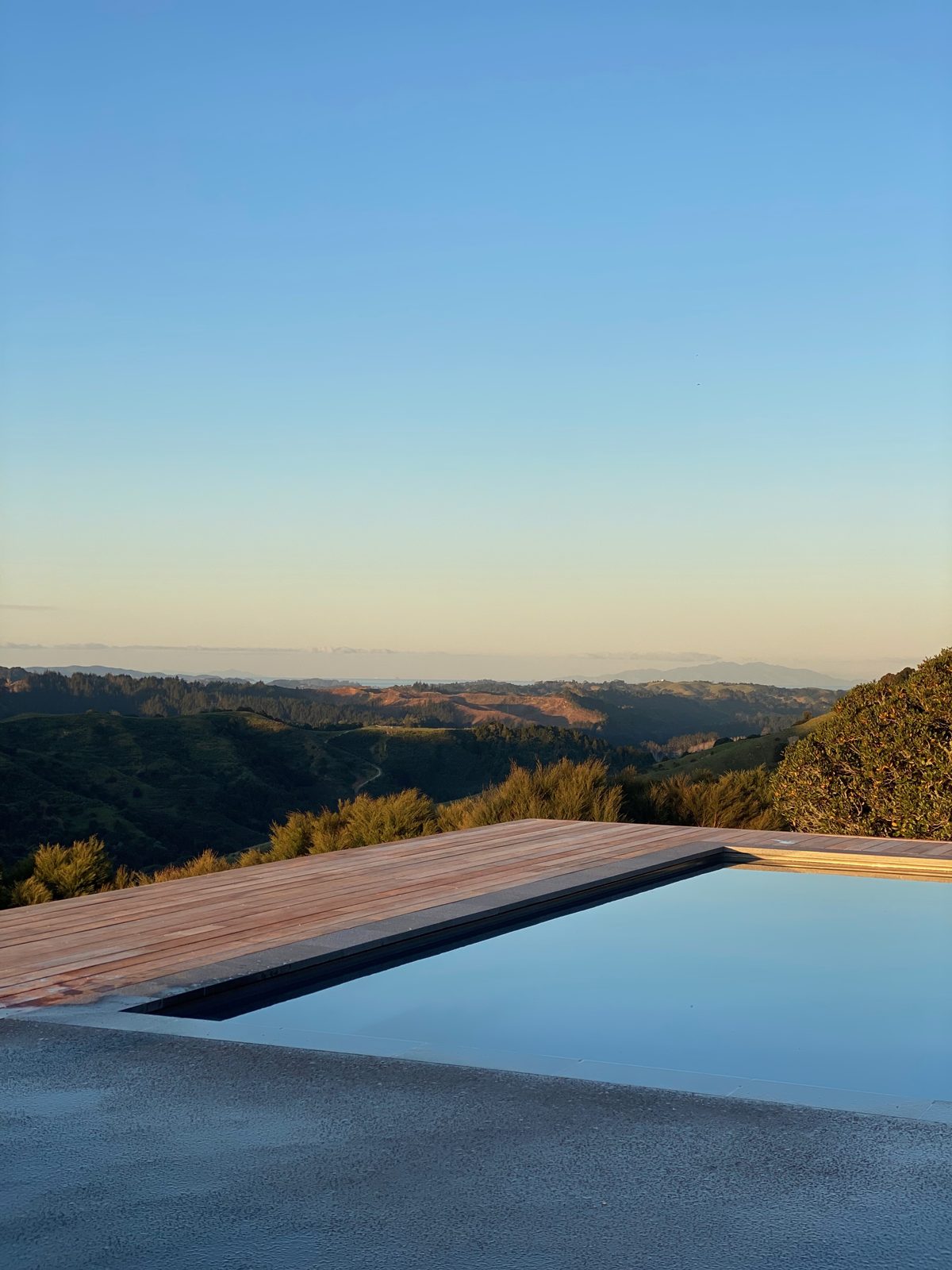 Timber decking along the edge of a swimming pool at dusk, with hills in the distance