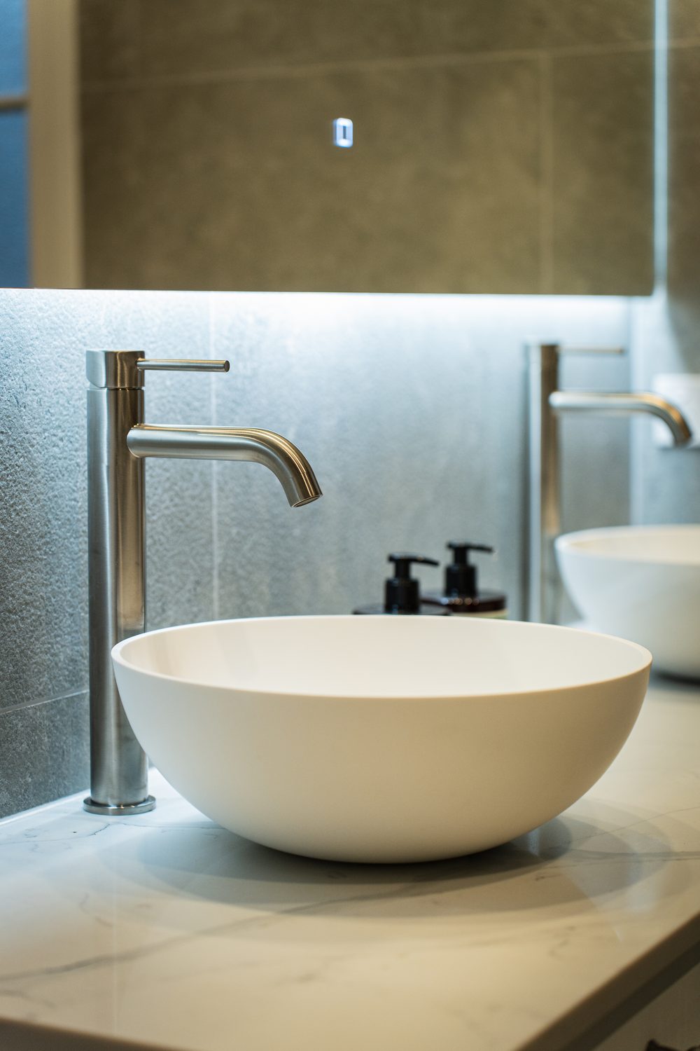 Round vessel basin with a tall brushed mixer on a stone vanity top
