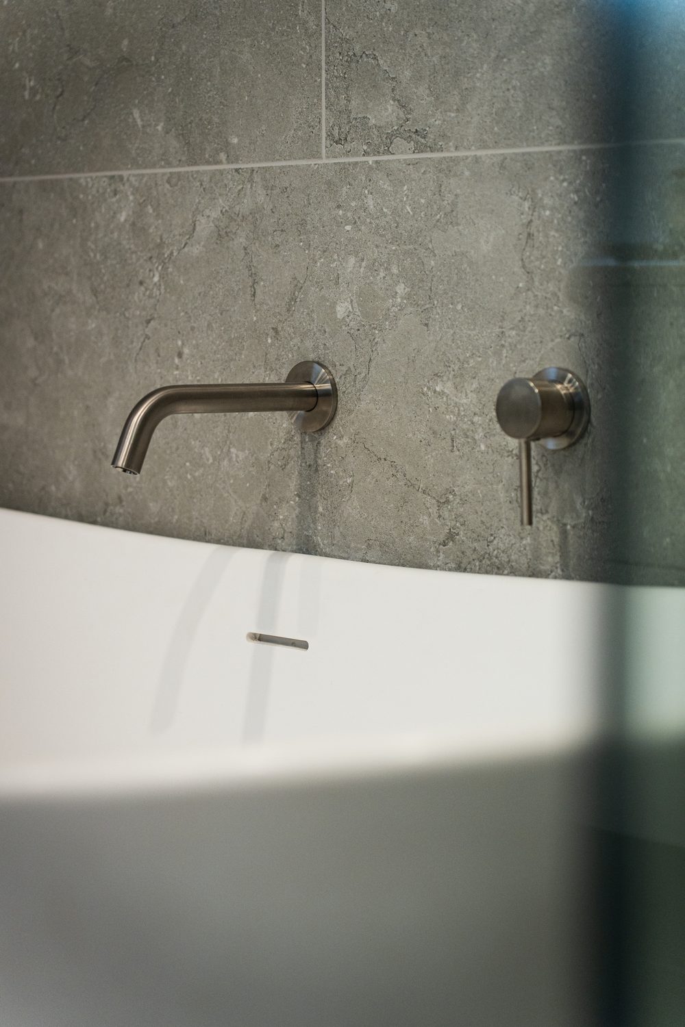 Detail of a brushed wall-mounted bath spout and mixer above a freestanding bath