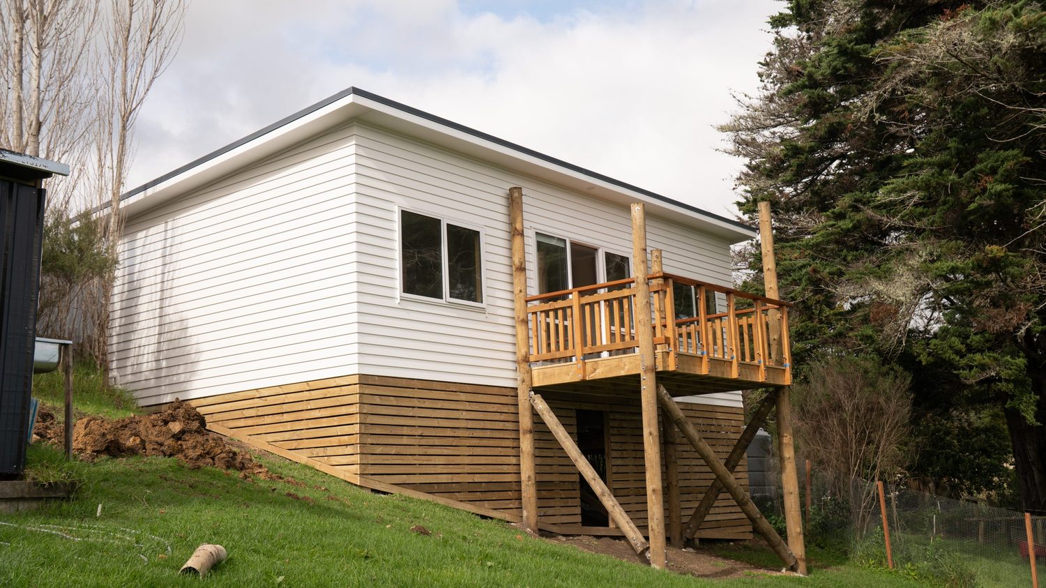 Raised timber deck with balustrade on the side of a white weatherboard house on sloping ground